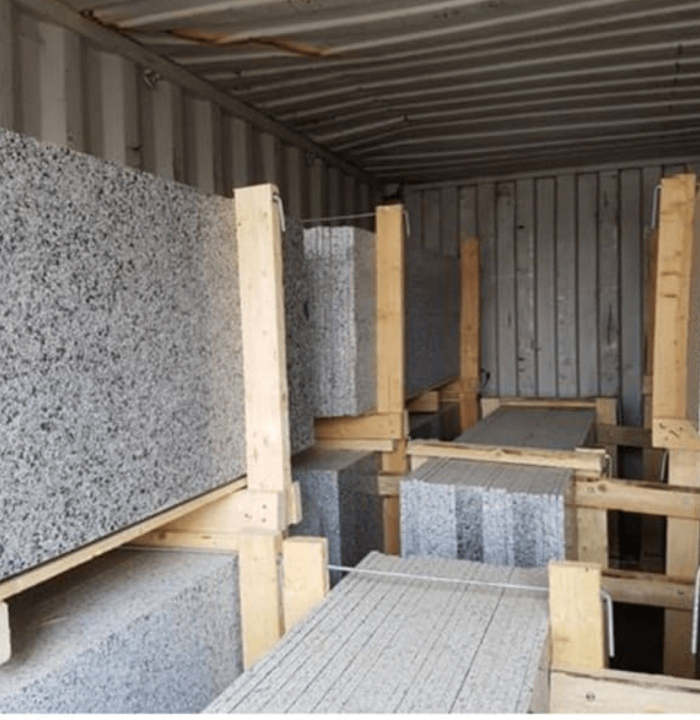 Stacked granite stone slabs secured with wooden supports inside a shipping container.