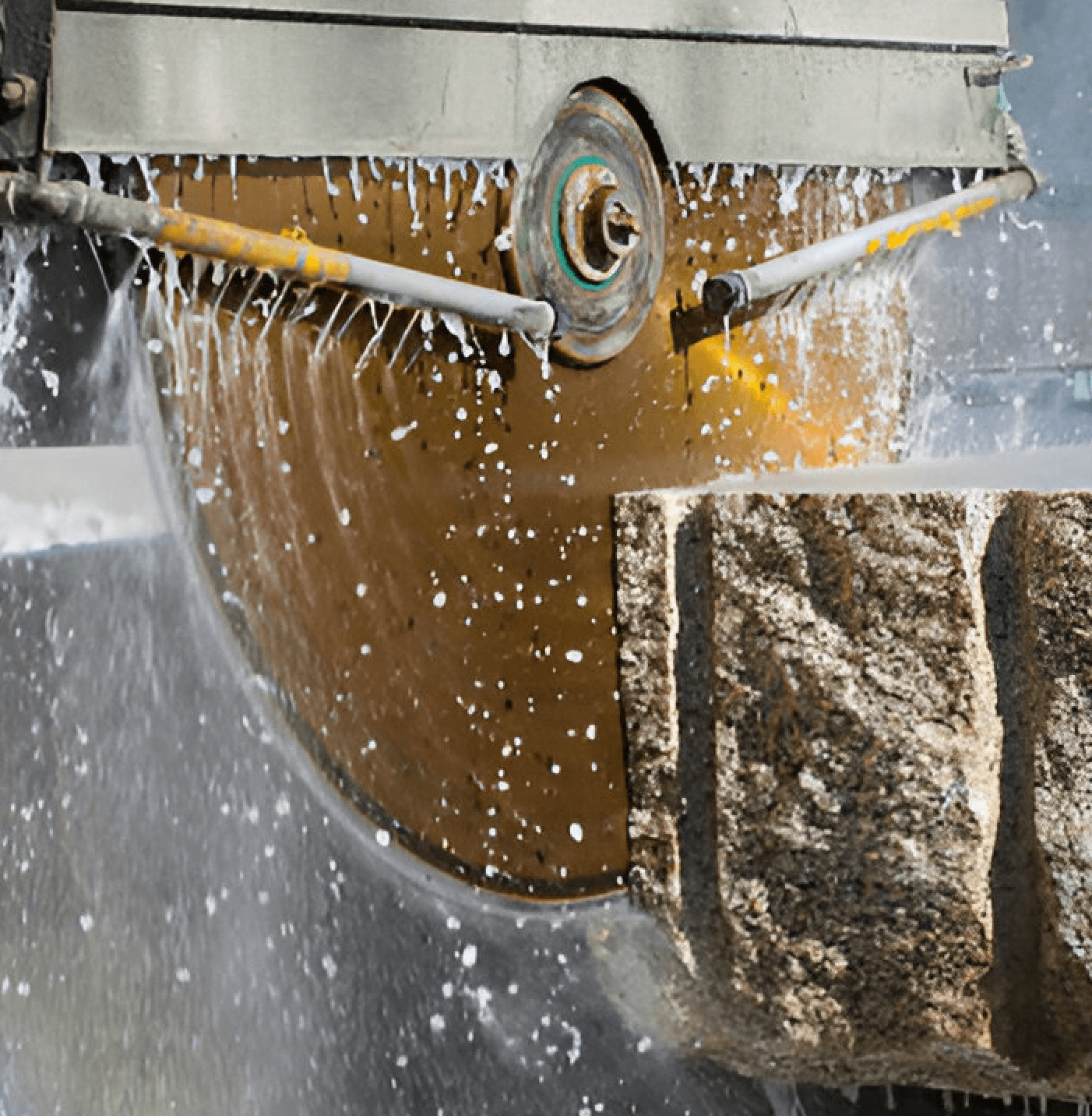 Close-up of a wet saw blade cutting a large stone block with water spraying.