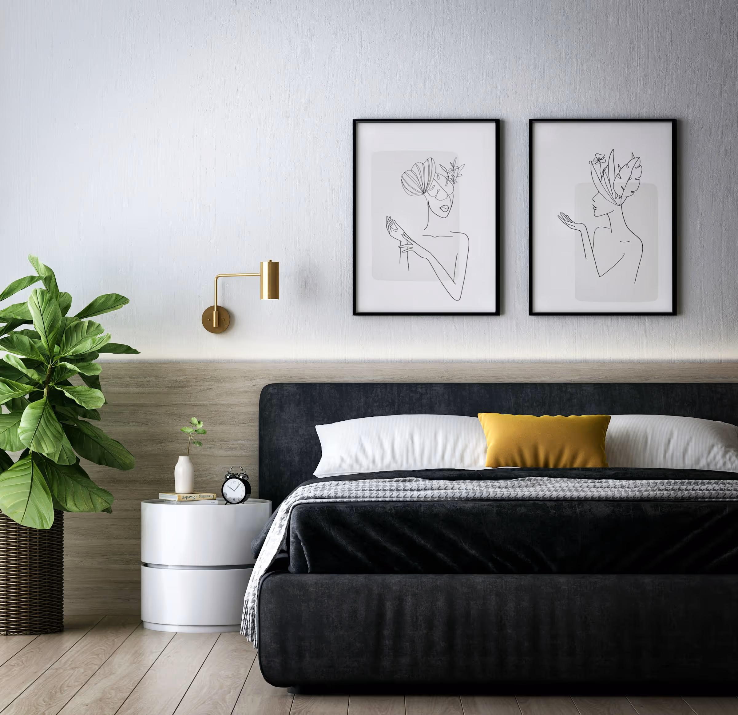 Modern bedroom with a black upholstered bed, white and yellow pillows, a small white nightstand with an alarm clock and plant, gold wall lamp, two minimalist line art portraits, and a large green potted plant.