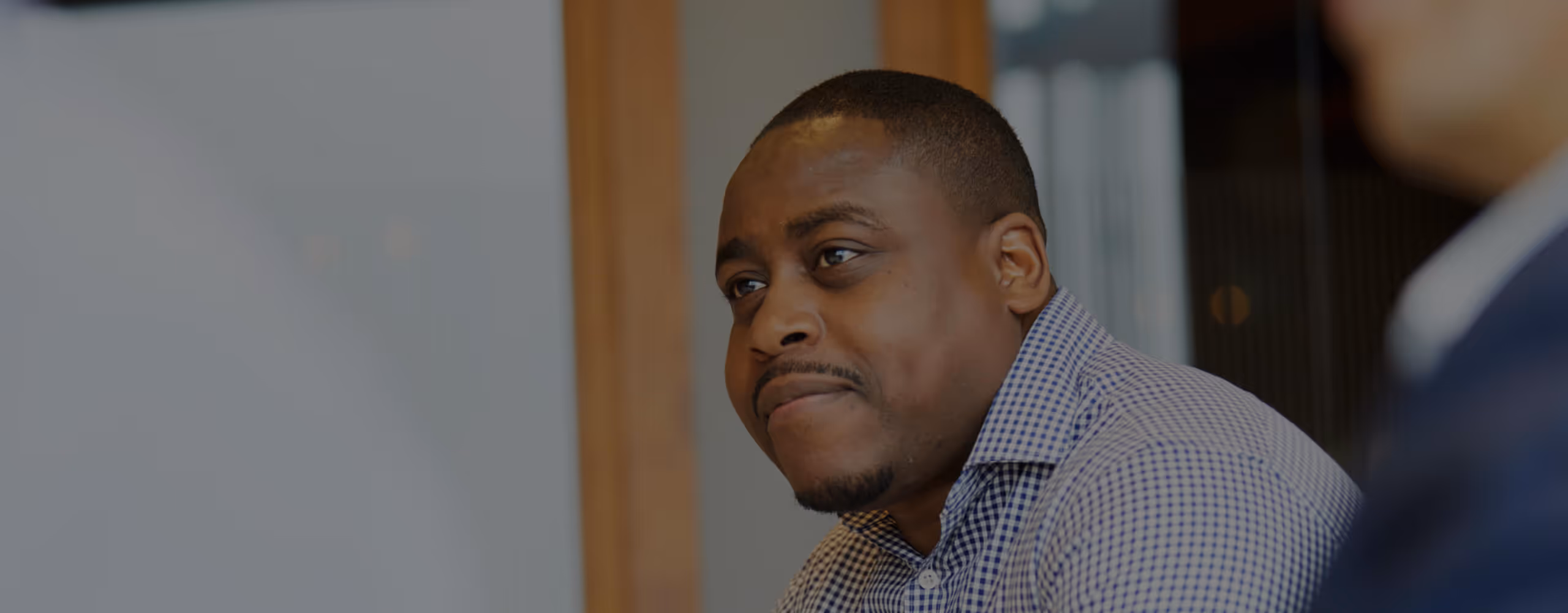 Close-up of a man in a checkered shirt attentively listening during a conversation indoors.