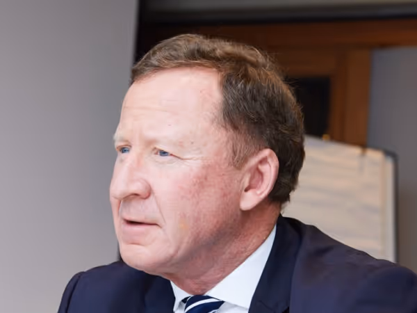 Middle-aged man with light brown hair wearing a navy suit and striped tie looking to the side.
