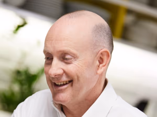 Smiling bald man wearing a white shirt in a bright indoor setting.