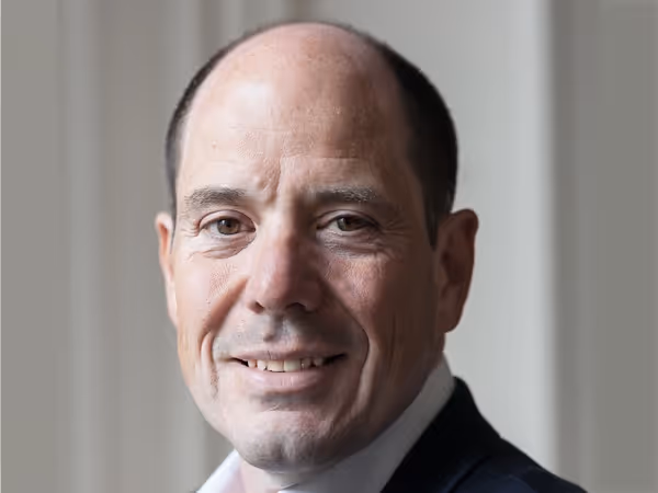 Portrait of a middle-aged man with short dark hair, wearing a dark jacket and white shirt, smiling slightly.