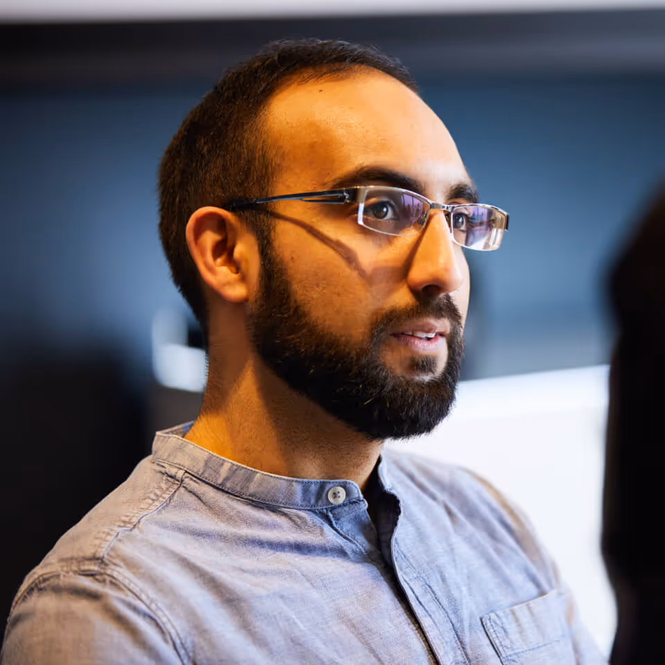 Bearded man wearing glasses and a light blue shirt looking attentively to the side.