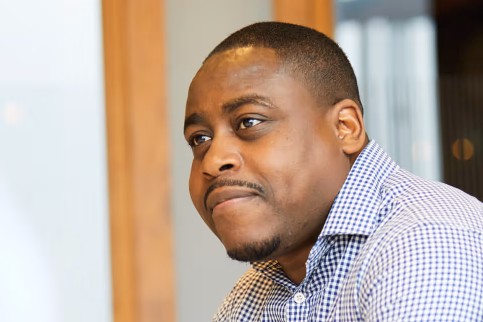 Close-up of a thoughtful man wearing a checkered shirt looking slightly to the side indoors.