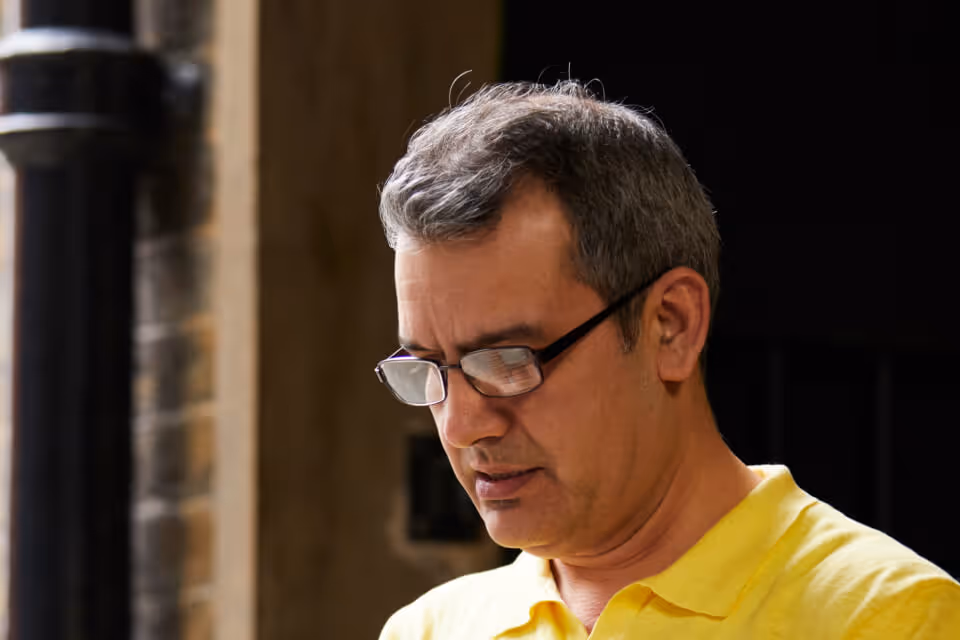 Middle-aged man wearing glasses and a yellow polo shirt looking down thoughtfully.