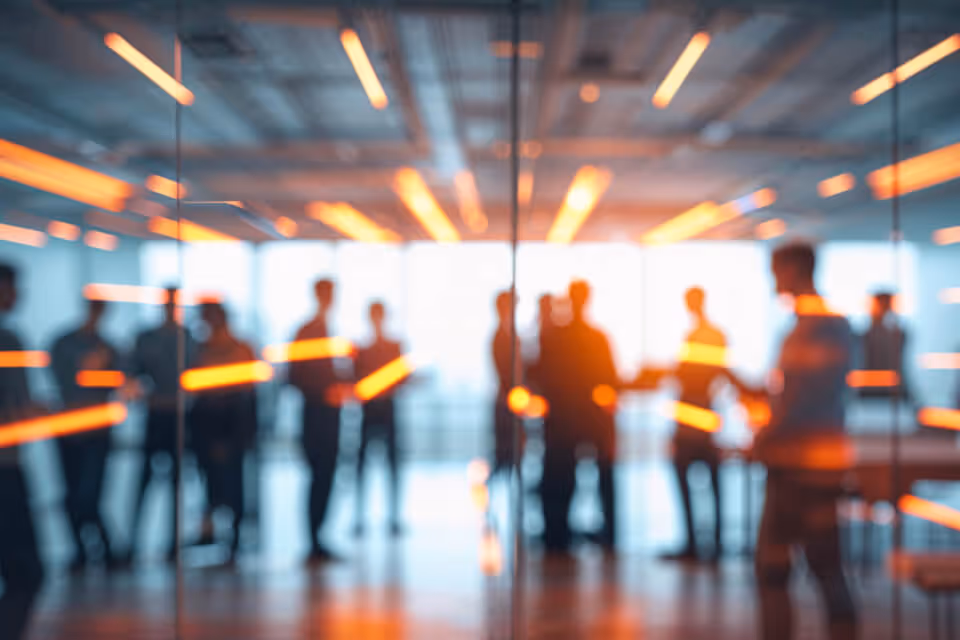 Blurry silhouettes of people standing and conversing in a modern office with orange light streaks across the image.