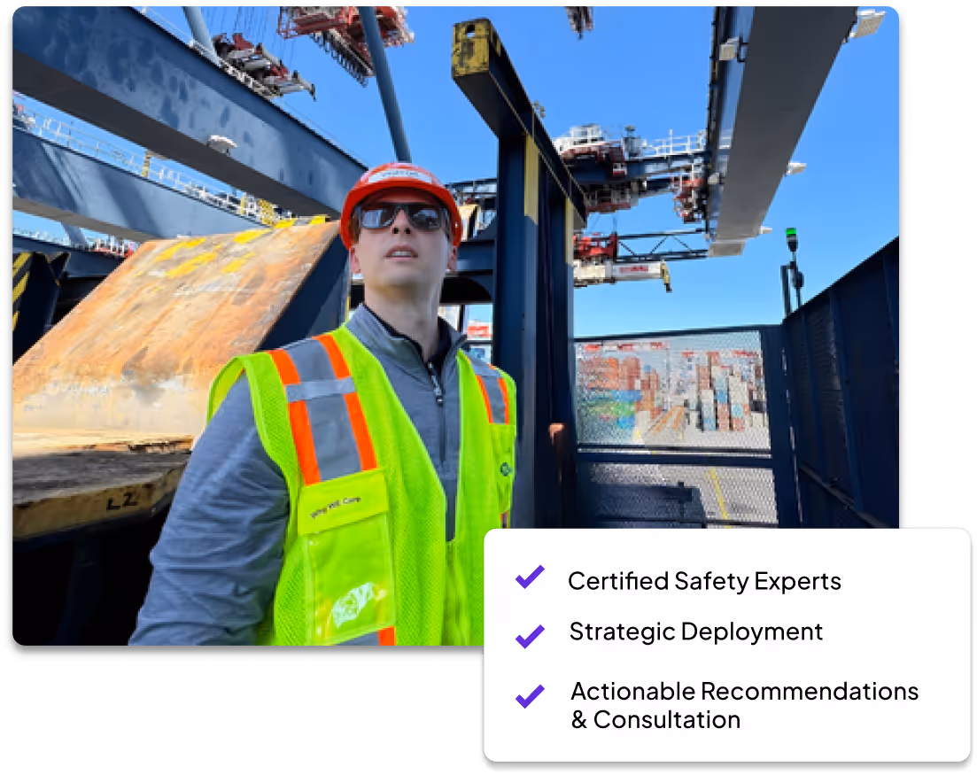 Construction worker wearing a red hard hat, sunglasses, and a neon safety vest at an industrial site with cranes and shipping containers.