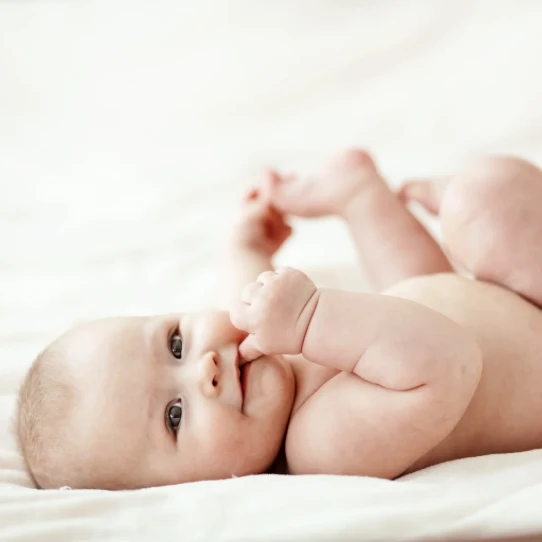 Bébé allongé sur le dos, regardant vers l'avant avec la main dans la bouche.
