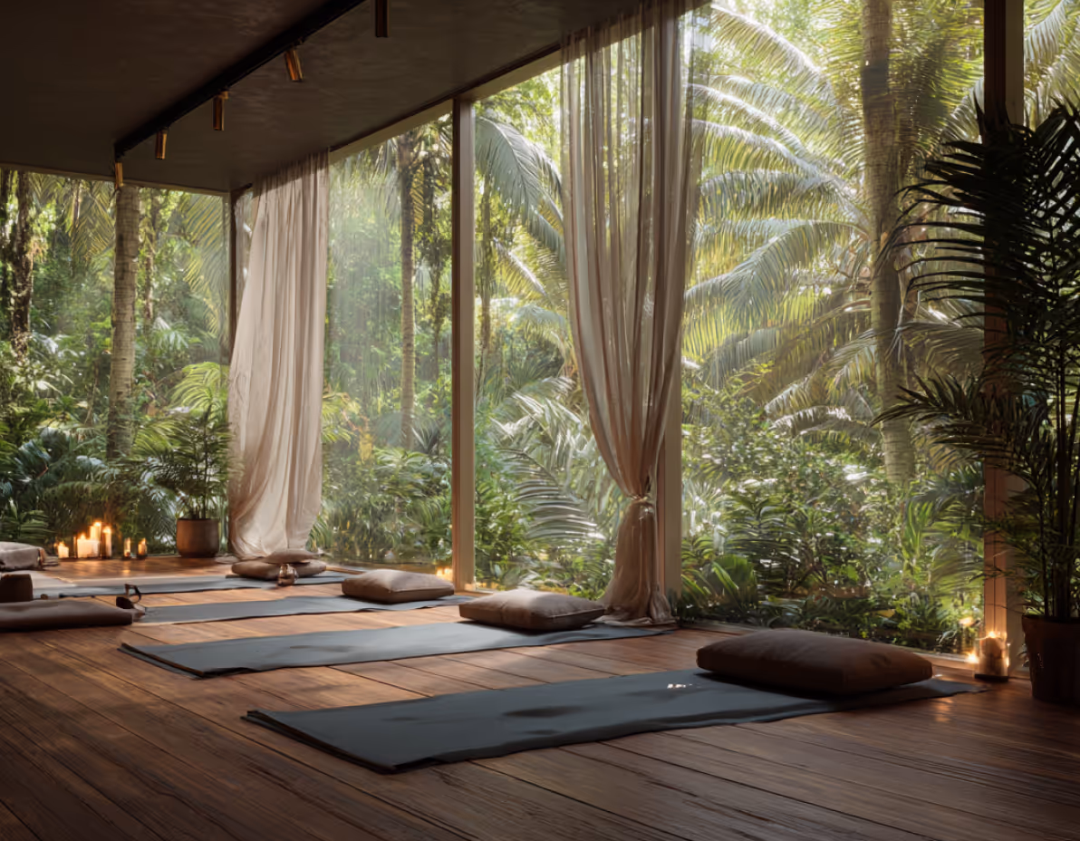 Serene yoga studio with wooden floor, cushions on mats, large glass windows overlooking lush tropical greenery, and lit candles.