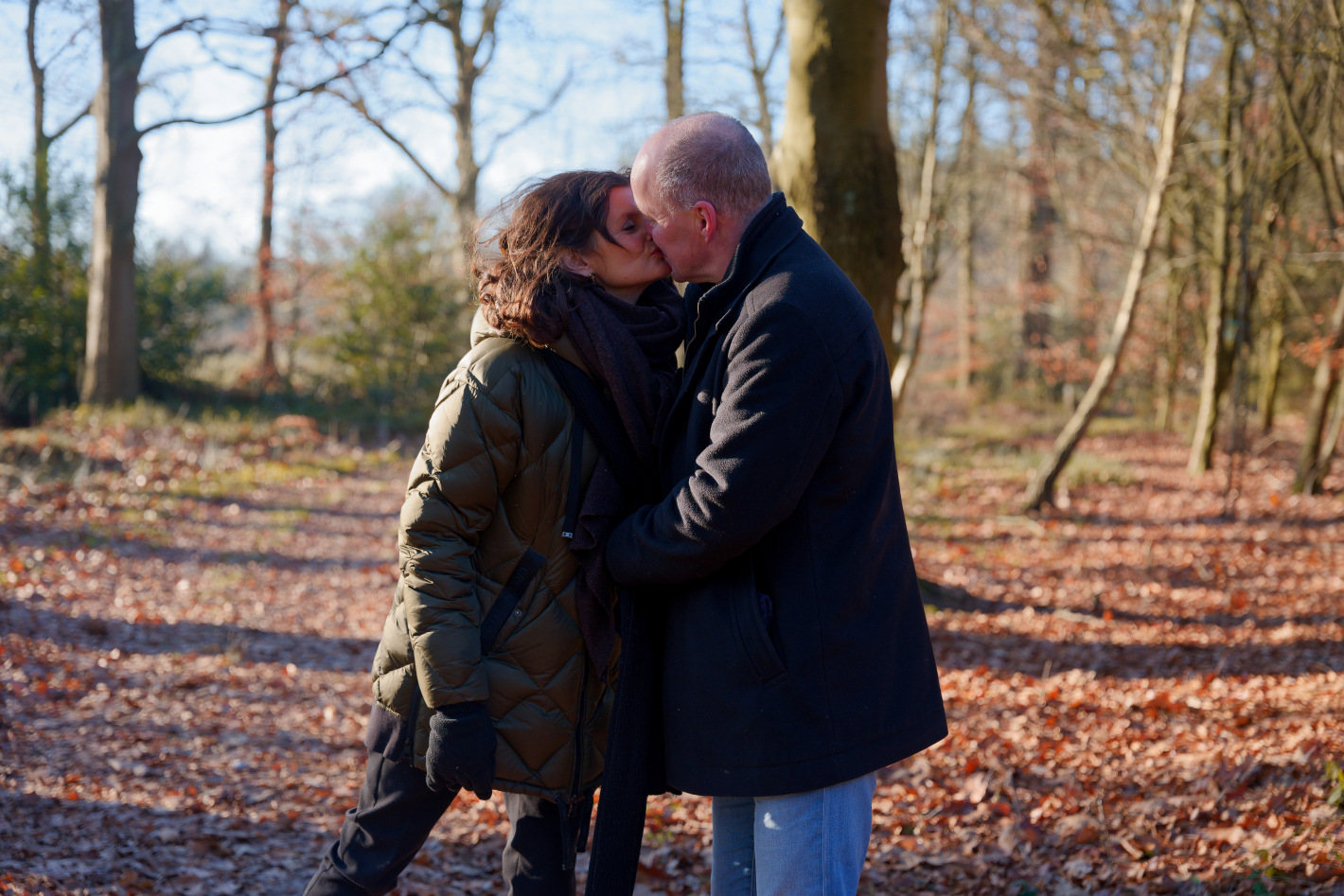 Koppel dat elkaar kust in een bos tijdens een zonnige herfst- of winterdag met vallende bladeren op de grond.