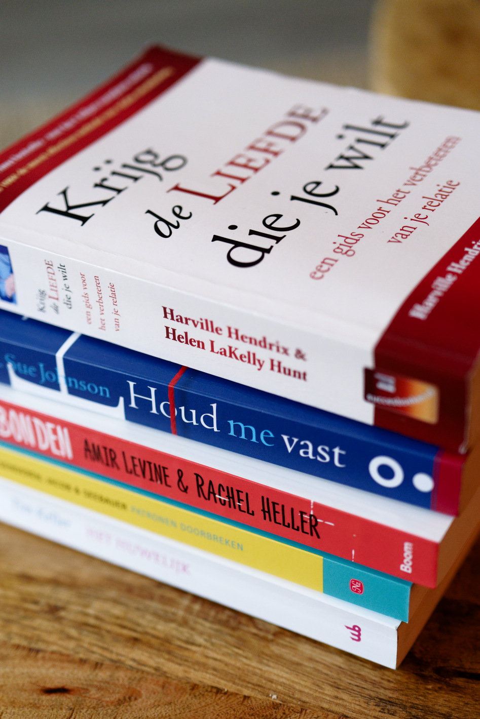 Stapeltje boeken op een houten tafel, bovenaan ligt het boek 'Krijg de liefde die je wilt' van Harville Hendrix en Helen LaKelly Hunt.