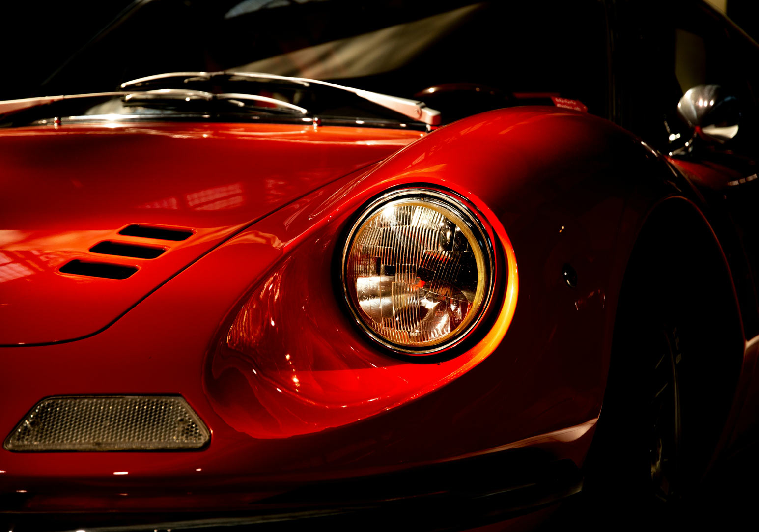 Close-up of the front left headlight and red hood of a classic sports car with ventilation slits.