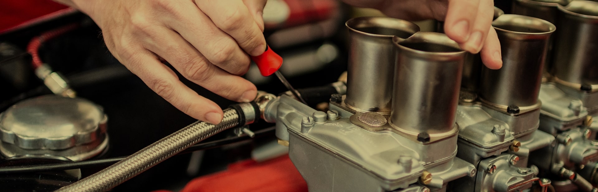 Close-up of hands using a small red tool to adjust a metallic engine component with cylindrical parts.