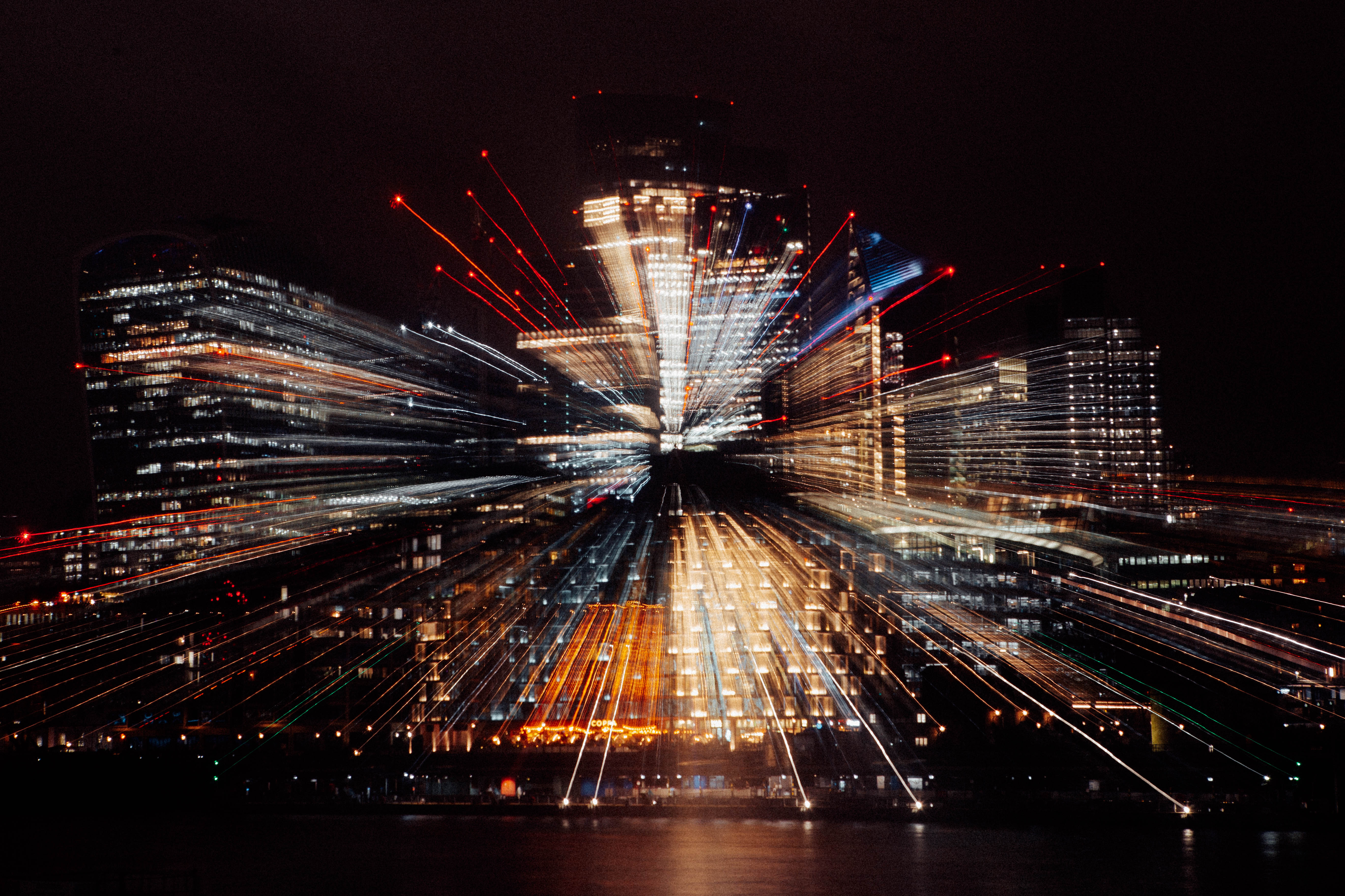 City skyline at night with light trails radiating outward from buildings, creating a zoom blur effect.