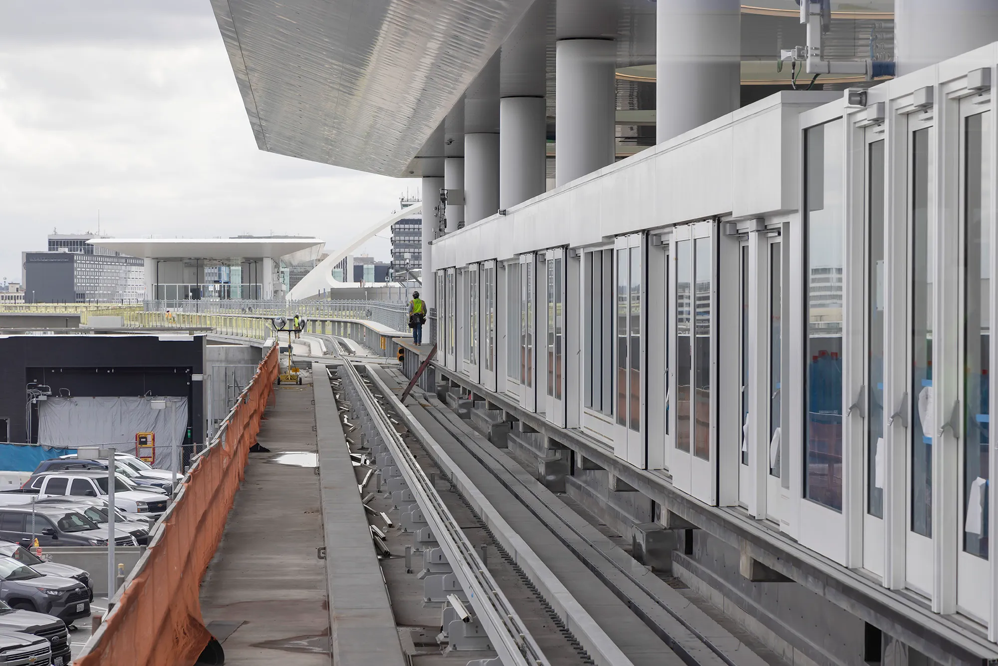 Construction worker walking on a platform near rails beside a modern building with glass doors and columns.