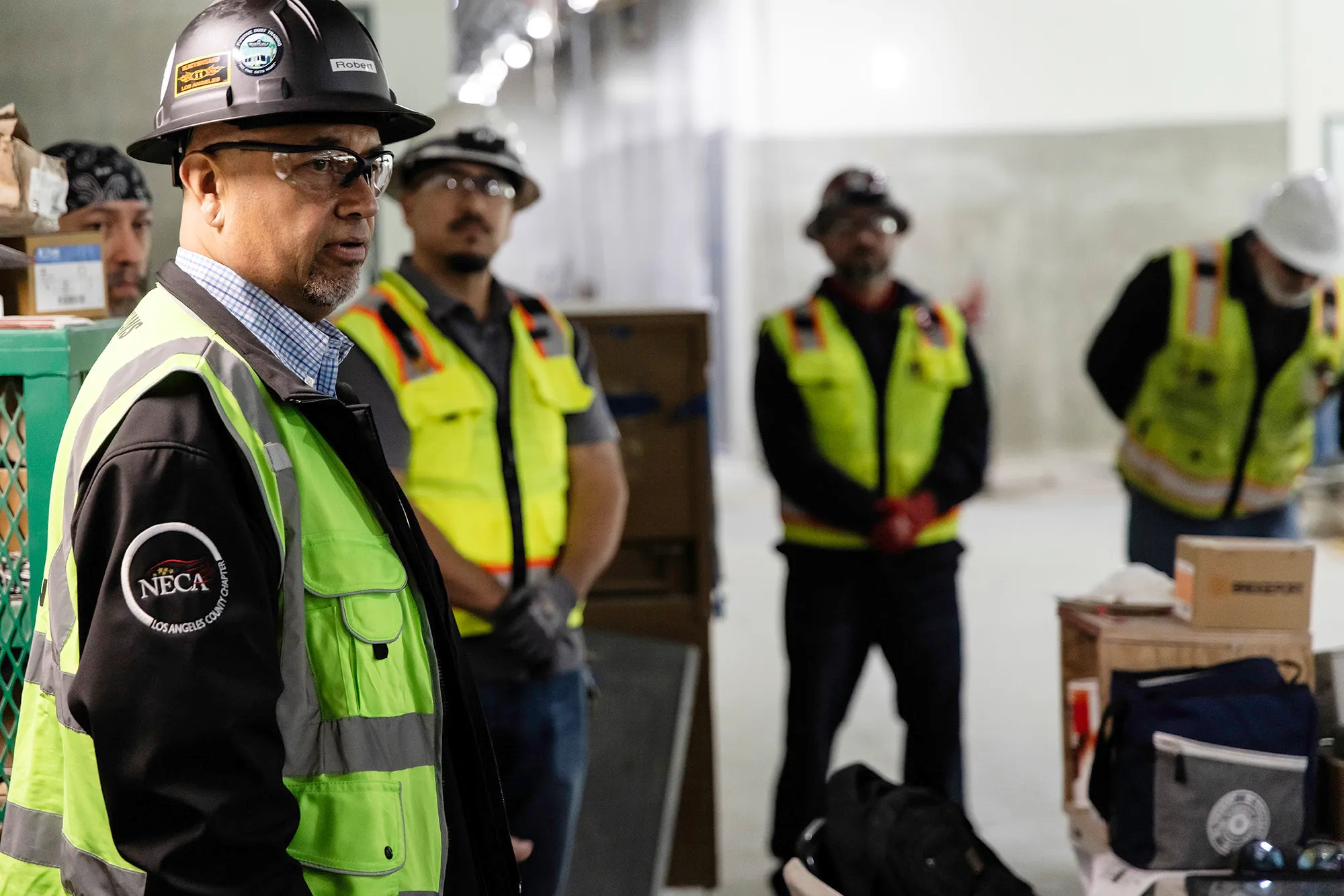 Construction workers wearing safety vests and helmets standing indoors in a worksite area.