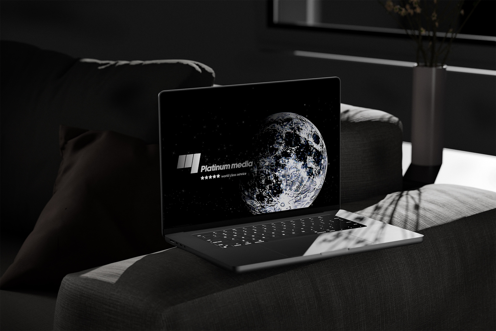 Modern laptop on a gray fabric couch displaying a digital image of the moon with text 'Platinum media' and 'world class service' alongside five stars on its screen in a dimly lit room.