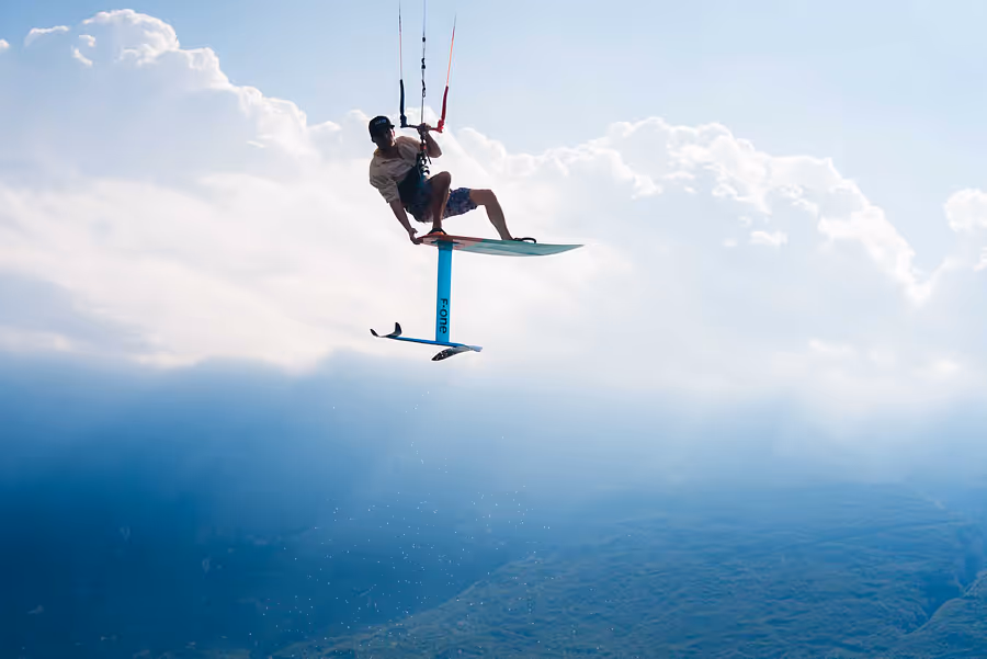 Person kitet auf einem Foil-Board über dem Wasser vor bewölktem Himmel.