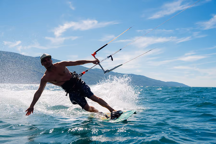 Ein Mann kitesurft auf dem Gardasee bei sonnigem Wetter mit Bergen im Hintergrund.