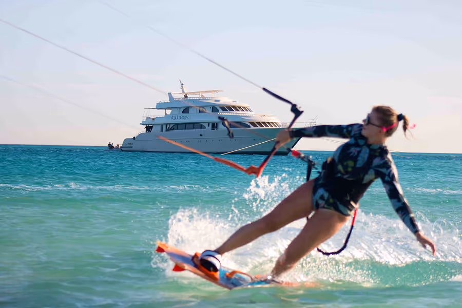 Frau in Neoprenanzug beim Kitesurfen auf dem Meer mit einer großen weißen Yacht im Hintergrund.
