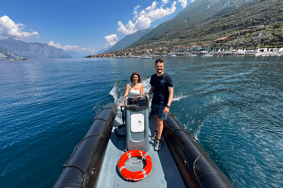 Ein Mann und eine Frau auf einem schwarzen Schlauchboot fahren auf einem See mit Bergen und blauem Himmel.