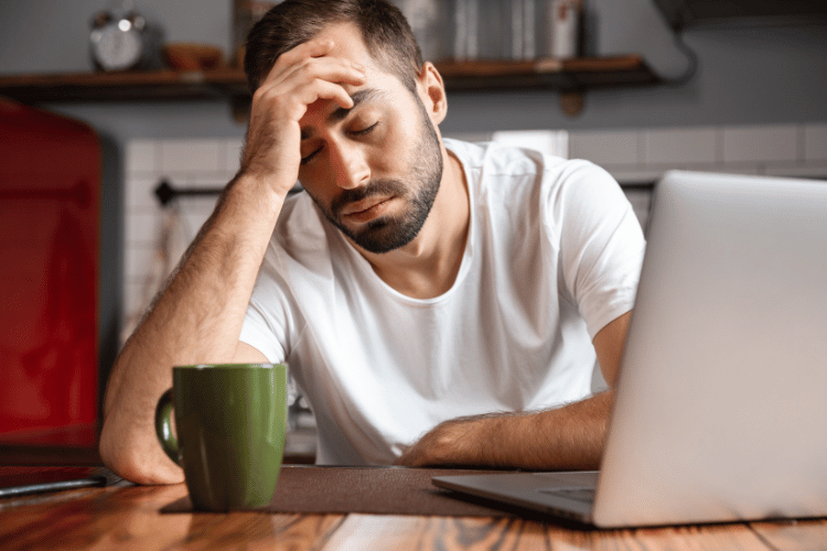 Tired man sitting at a laptop with his hand on his forehead.