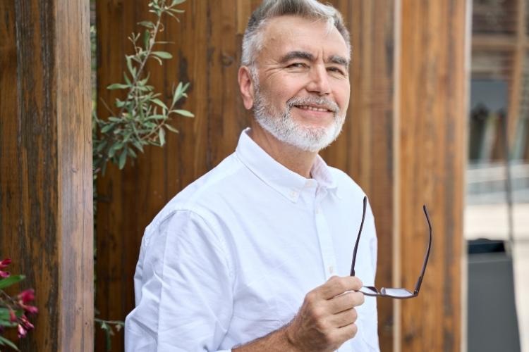 Grey-haird man in white shirt holding glasses.
