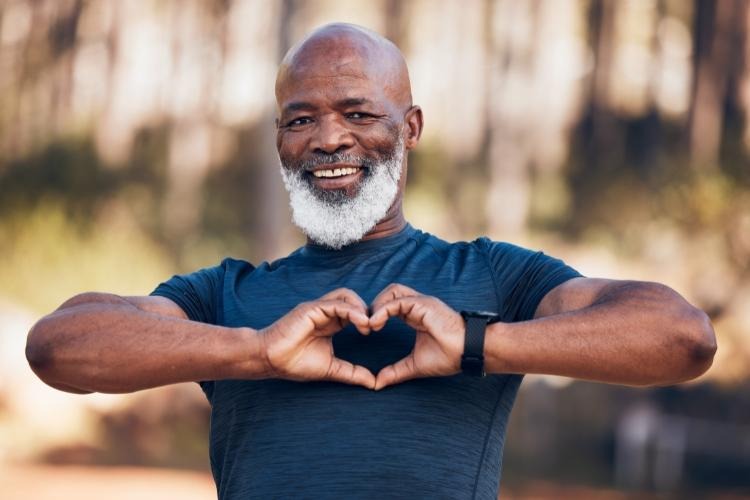 Man with grey beard in a blue T-shirt making the heart sign with his hands