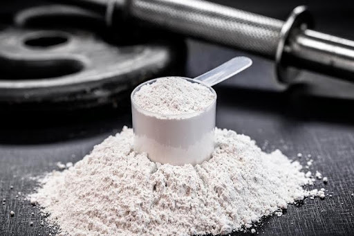 Scoop of creatine powder beside weightlifting equipment.