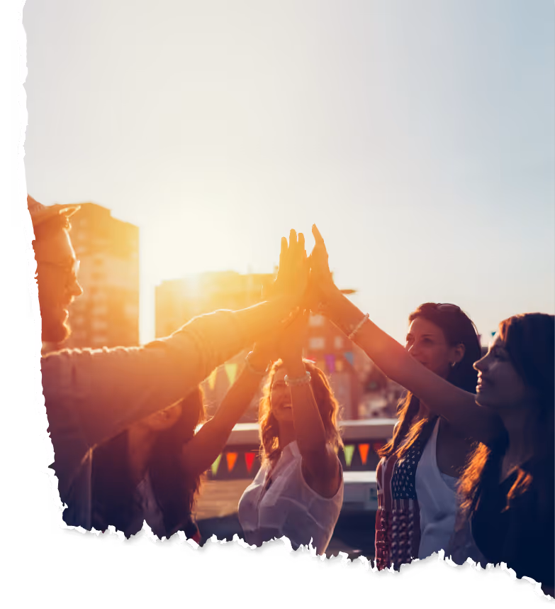Groupe de personnes donnant un high five ensemble au coucher du soleil en extérieur, avec des bâtiments en arrière-plan.