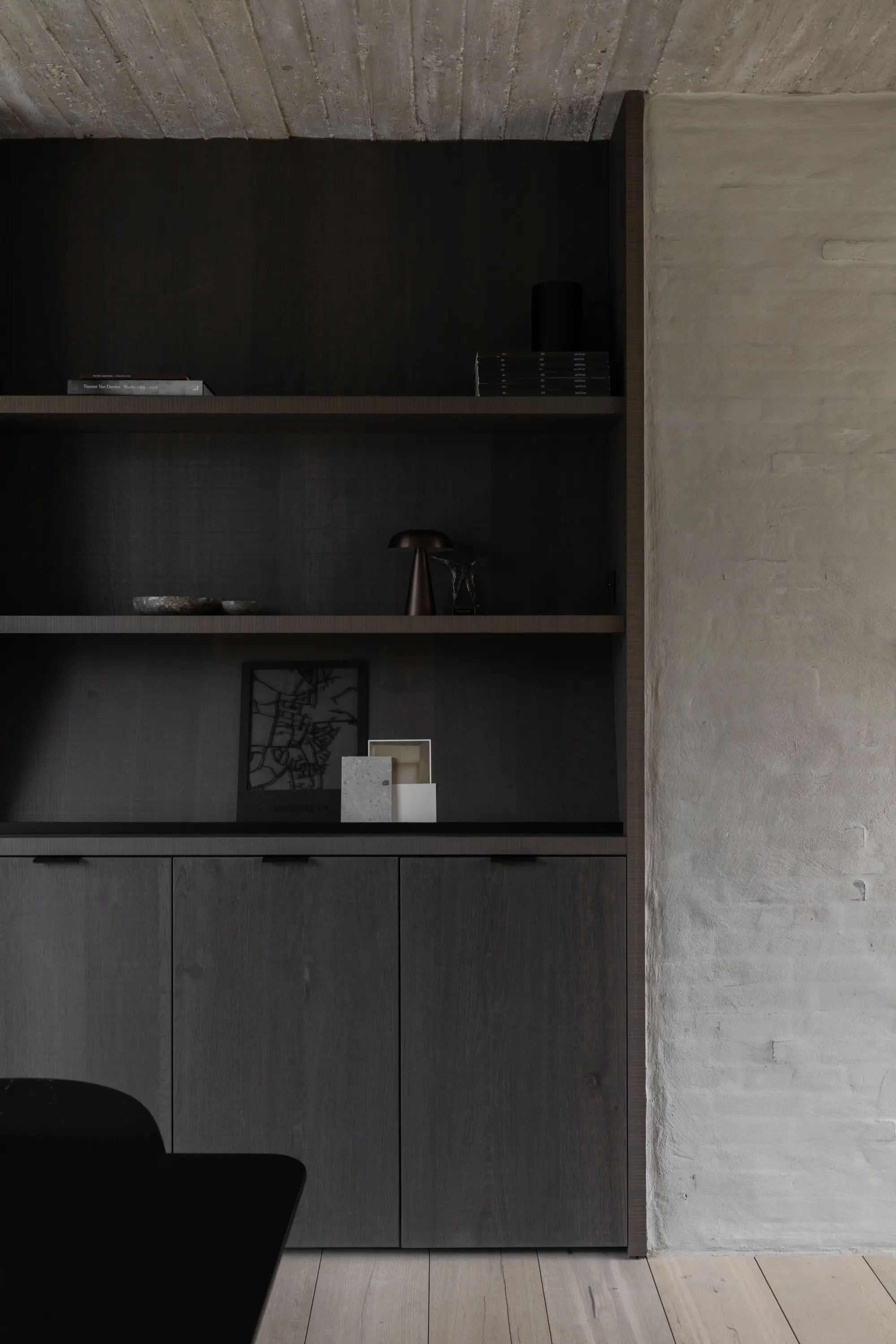 Donkere houten kast met open planken tegen een betonnen muur en een licht houten vloer.