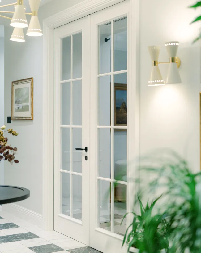 White double glass-paneled doors in a bright room with indoor plants and framed artwork.