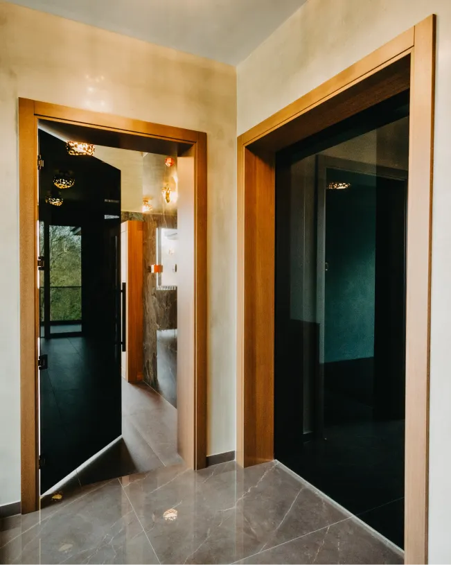 Interior view of two modern wooden doors with dark glass panels in a hallway with beige walls and marble flooring.