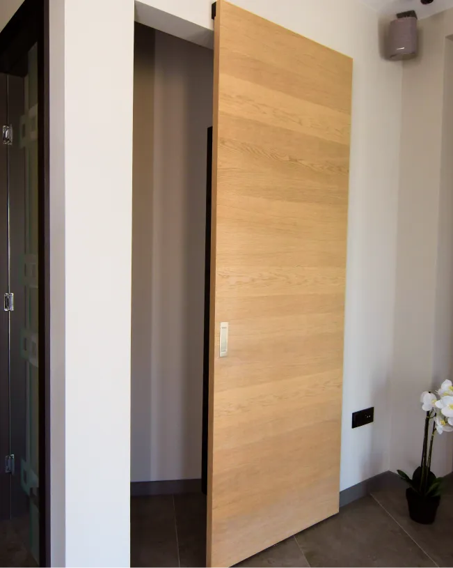 Light wood sliding door partially open in a modern interior with tiled floor and white walls.