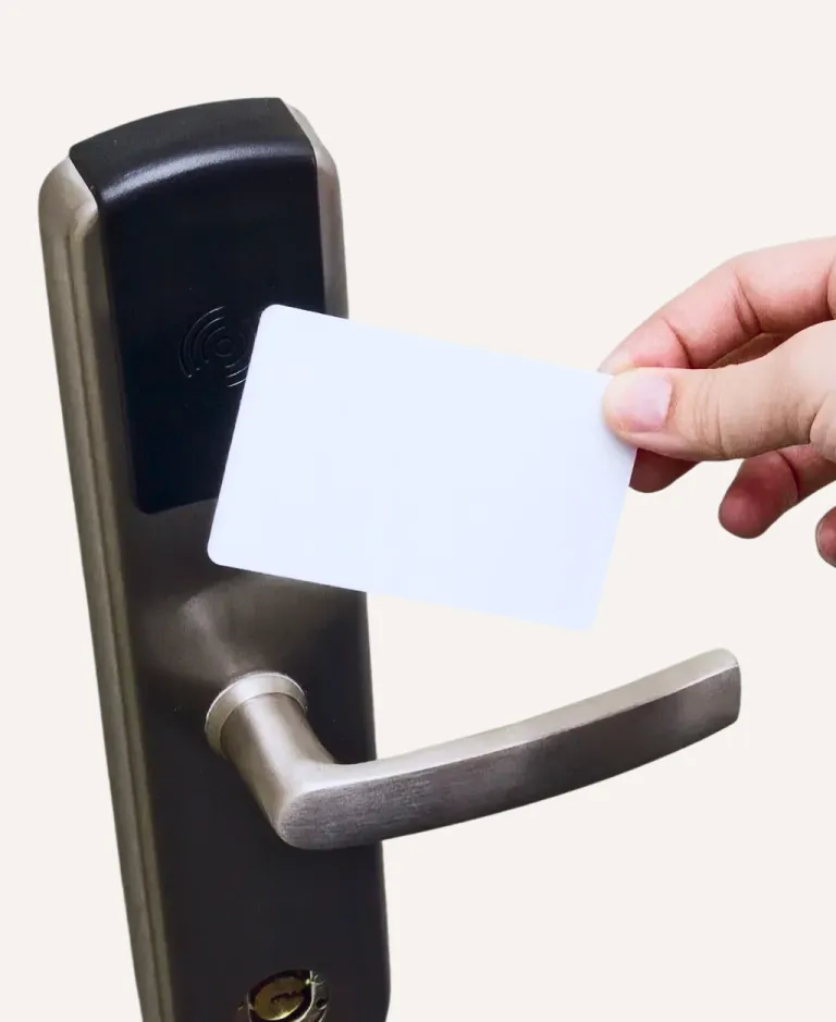 Hand holding a white key card near an electronic door lock with a metal handle.