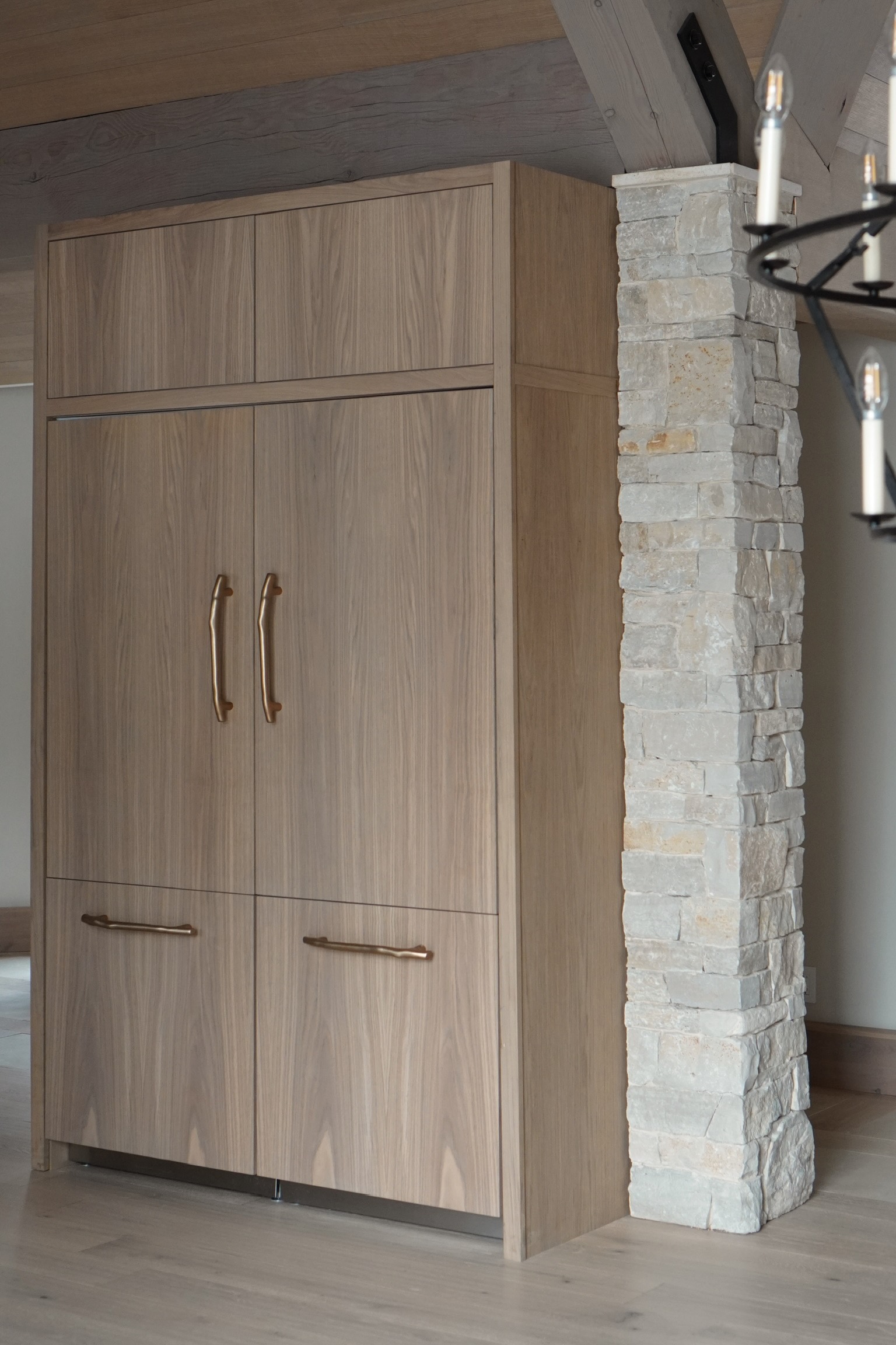 Custom wood panel ready refrigerator with brass hardware beside stone column, Lake Tahoe chalet