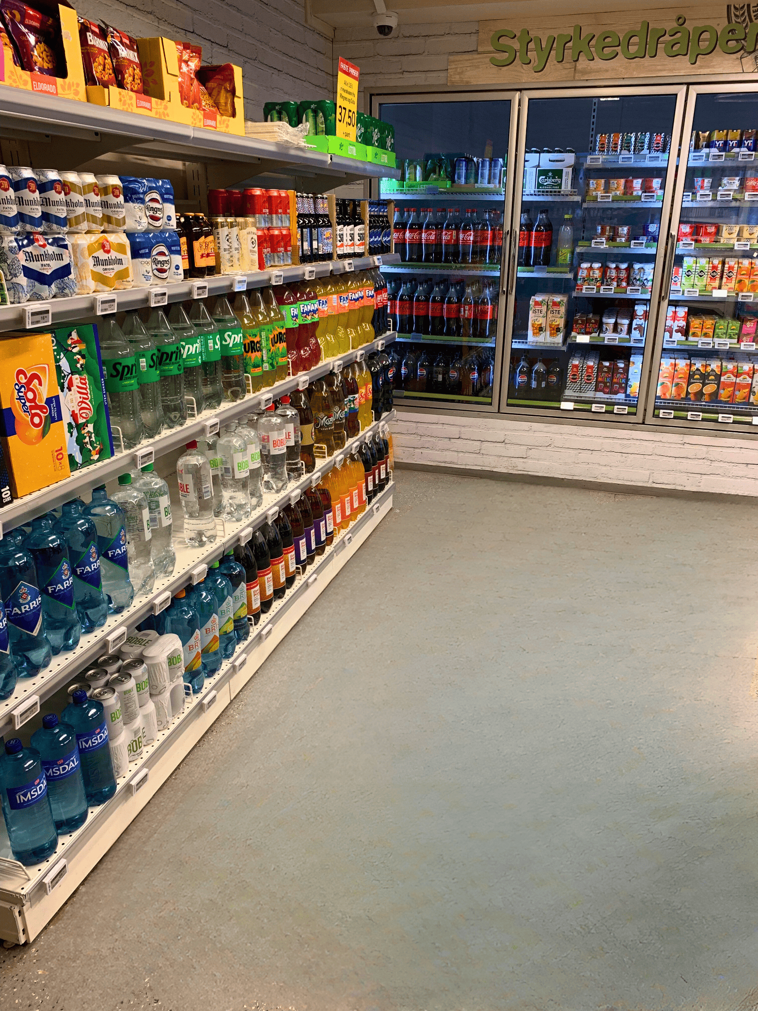 Gang med kjøledisker og hyller i en dagligvarebutikk, med tilbudskilt på veggen.