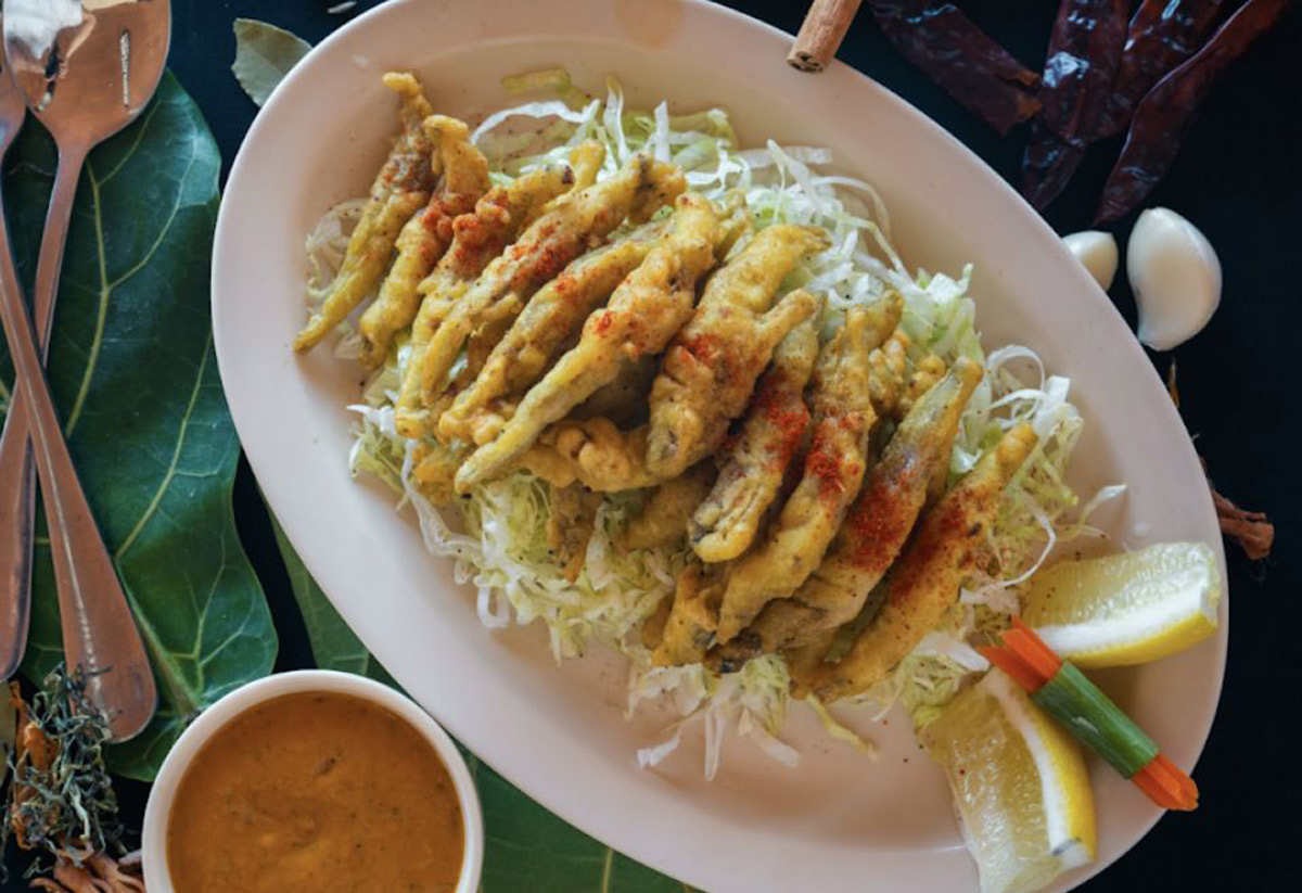 Plate of crispy fried okra on shredded lettuce, garnished with paprika, lemon wedges, and vegetable sticks. Served with a side of dipping sauce.