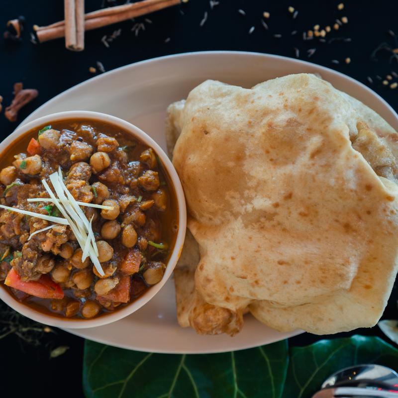 Plate with a bowl of flavorful chickpea curry garnished with julienned ginger, alongside a large piece of fluffy, golden-brown bread. Warm, inviting tone.