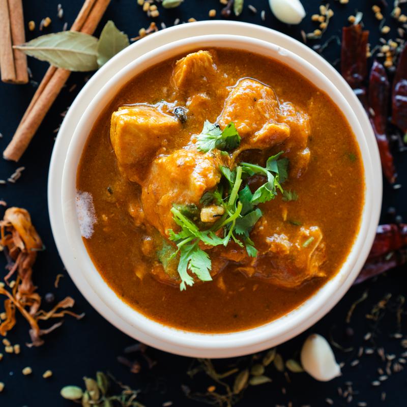 A vibrant bowl of spicy curry with tender chicken pieces, garnished with fresh cilantro. Surrounding spices enhance the warm, aromatic ambiance.