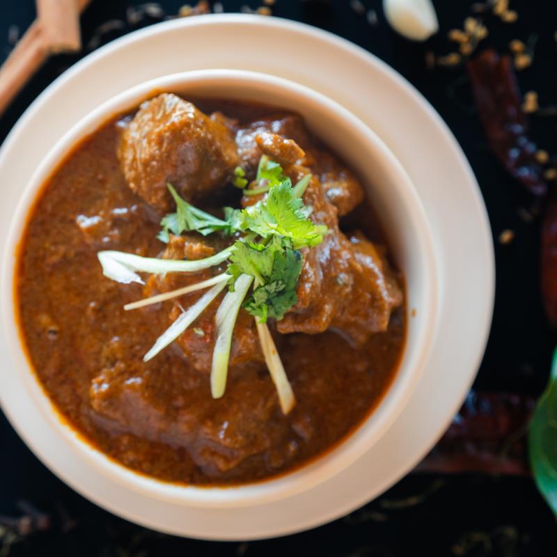 A bowl of rich brown curry with chunks of meat, garnished with fresh cilantro and sliced ginger, creating a savory and aromatic presentation.