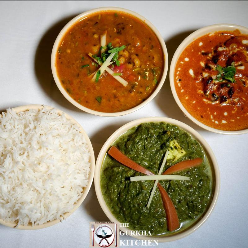 A top view of a meal with white rice, creamy lentil curry, tomato-based curry, and spinach paneer garnished with vegetables, set on a white tablecloth.