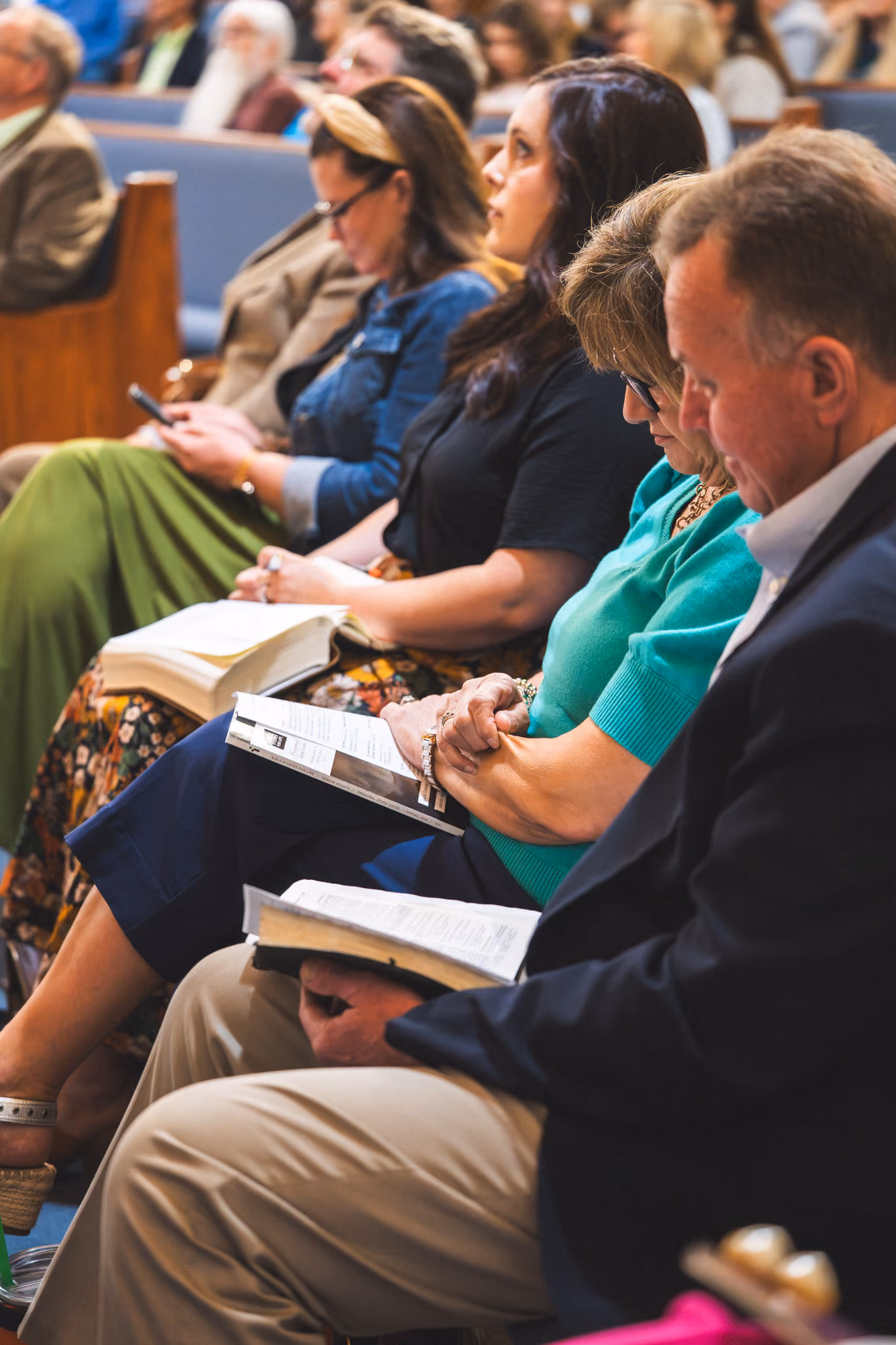 People seated in pews reading or praying in a church setting.