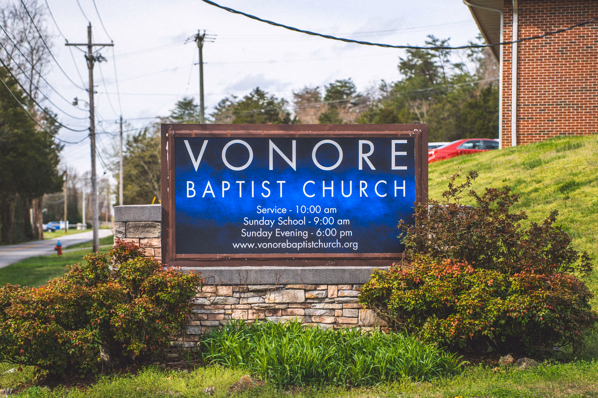 Sign for Vonore Baptist Church with service times and website, surrounded by bushes and grass.
