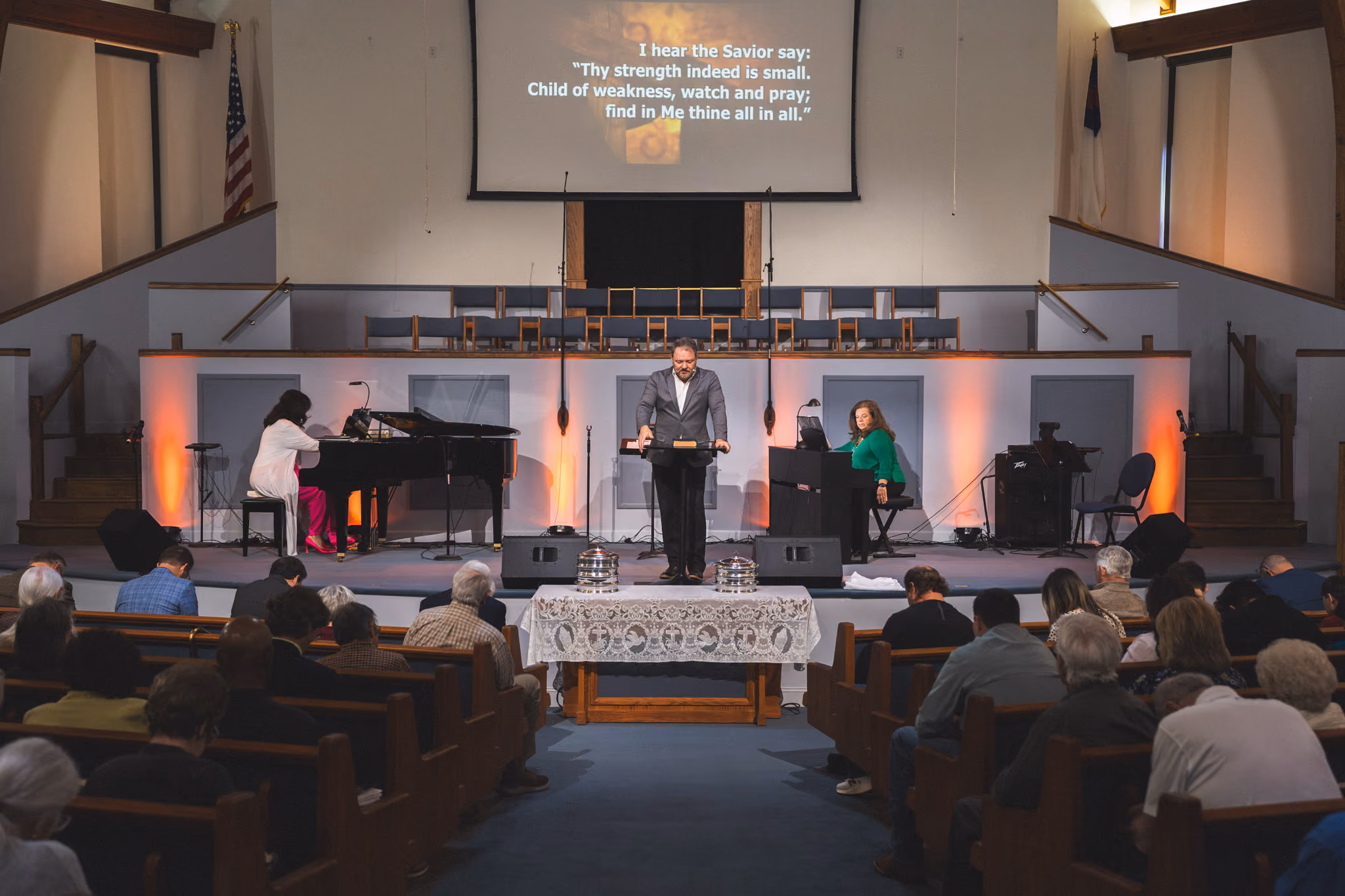 Man preaching at church podium with two pianists and congregation seated in pews.