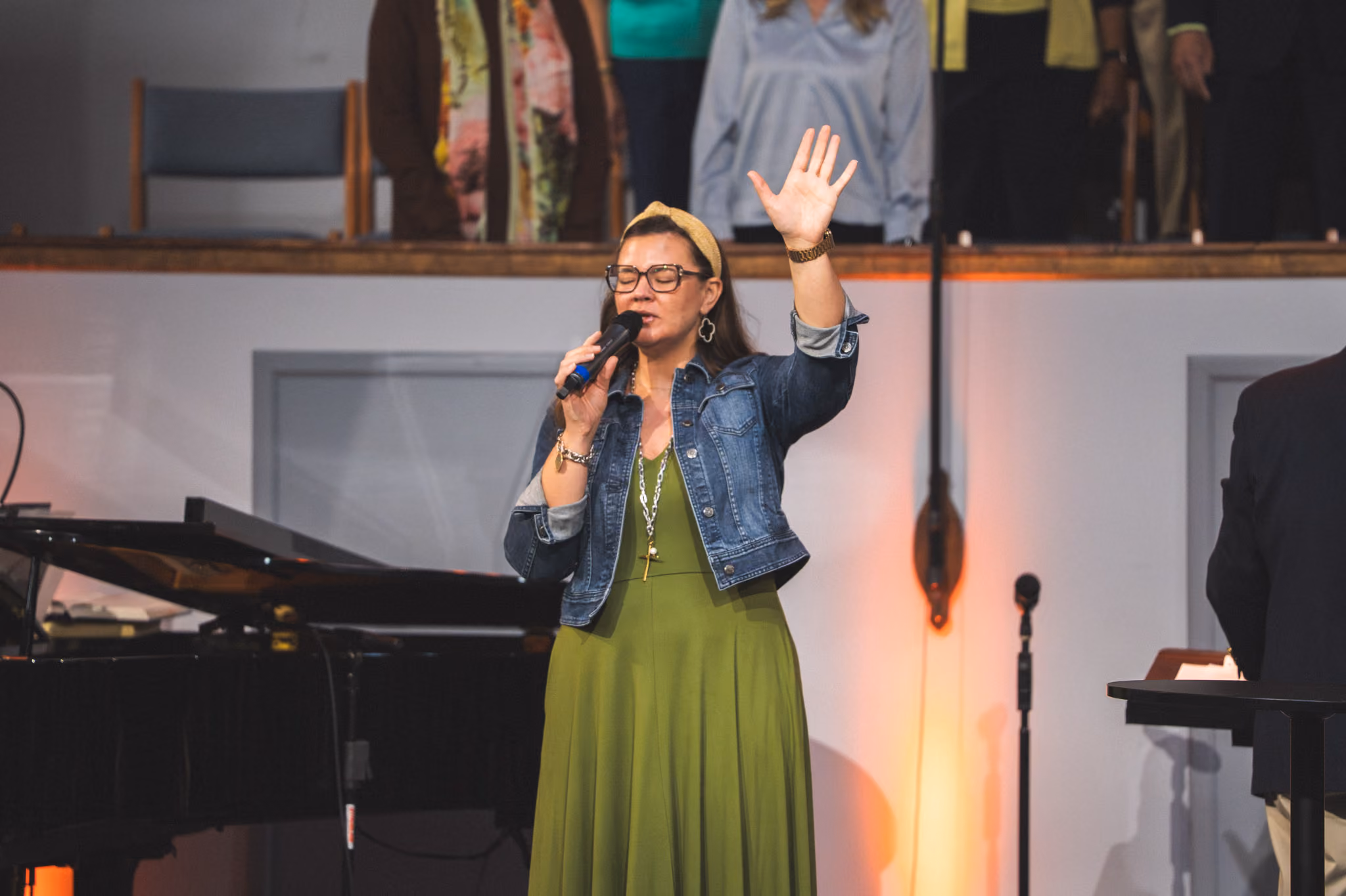 Woman with microphone and raised hand singing or praying on stage in a church setting.