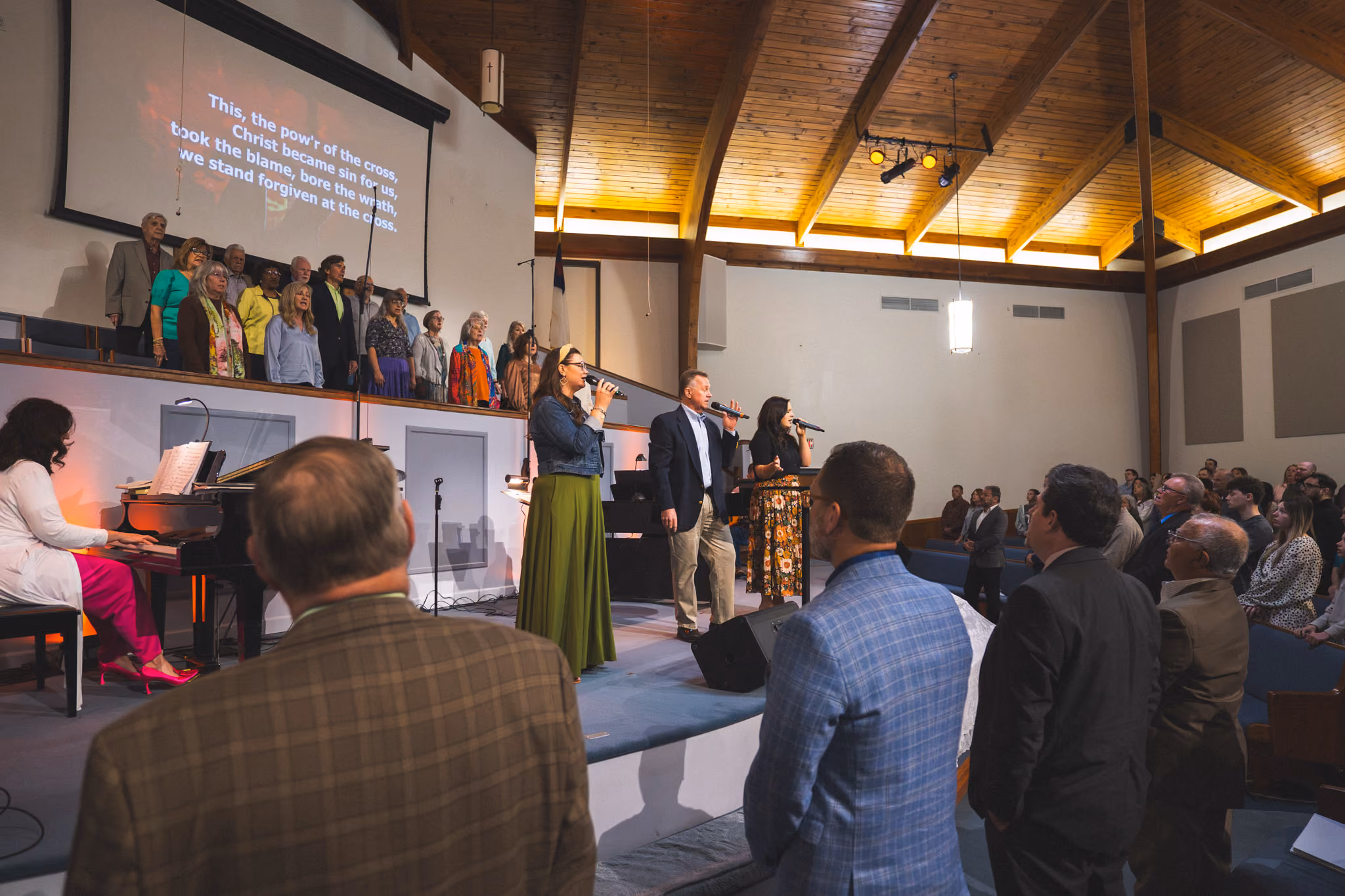 Congregation and choir singing in church with lyrics projected on screen and pianist playing.