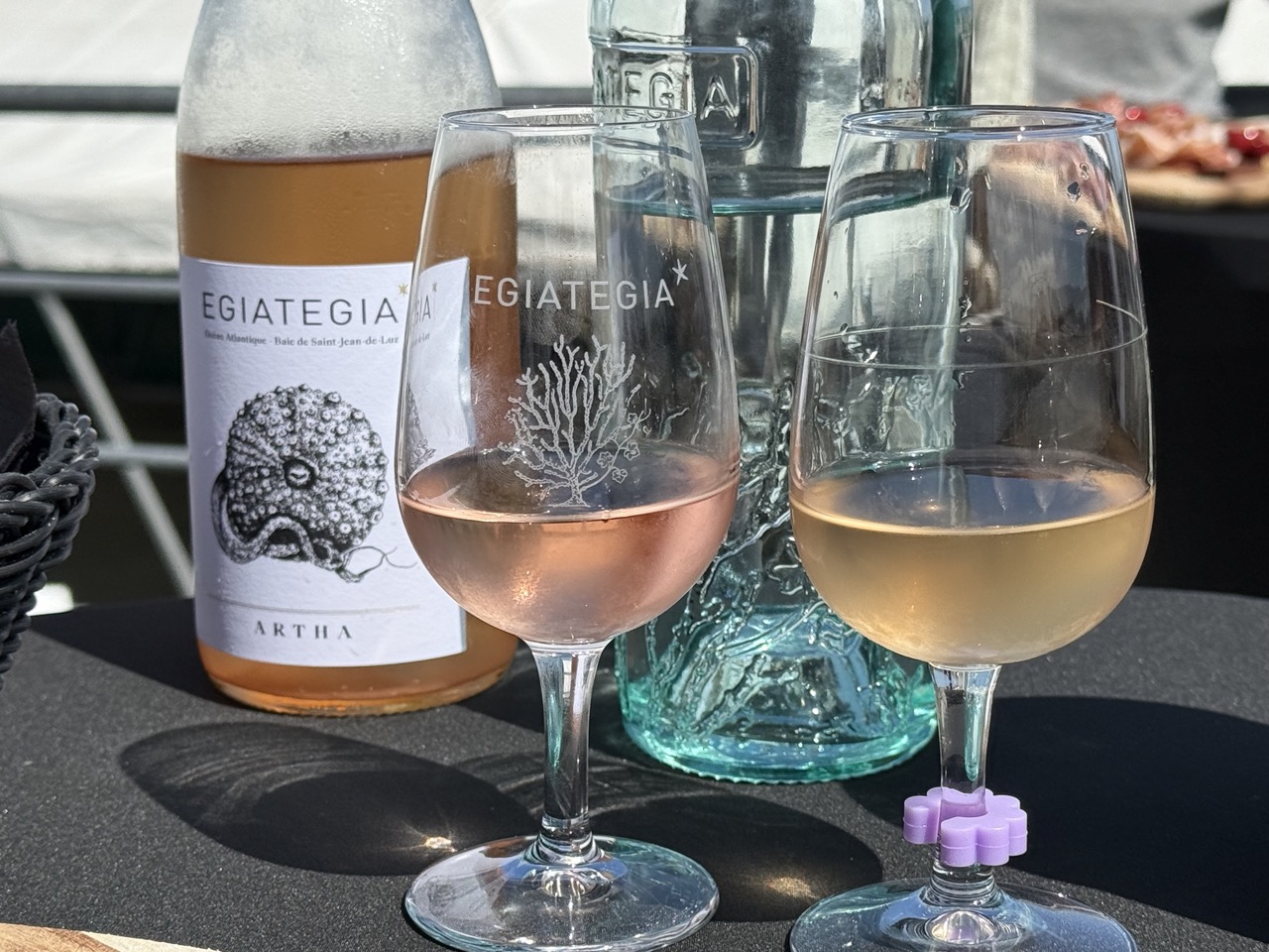 Glas Weißwein neben einem blauen Teller mit frischen Austern auf Eis und einer Zitronenscheibe.