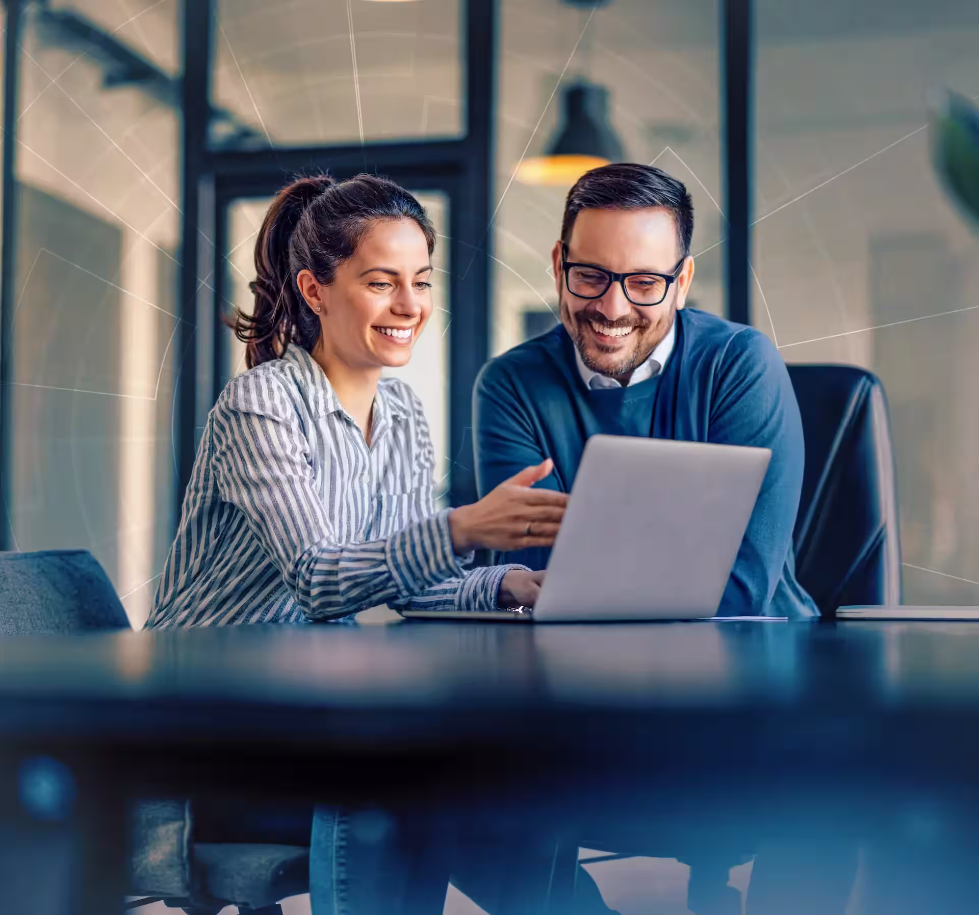 Two colleagues smiling and discussing while looking at a laptop in an office.